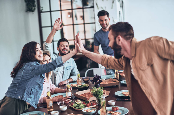 Young man and woman giving each other high-five while enjoying dinner party among friends - Photo, image