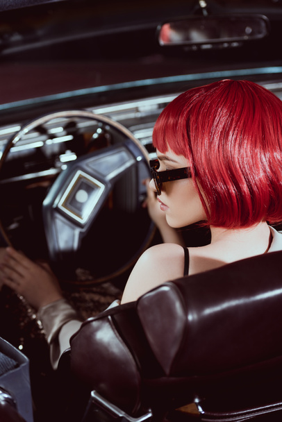 young woman in red wig and sunglasses driving retro car - Zdjęcie, obraz