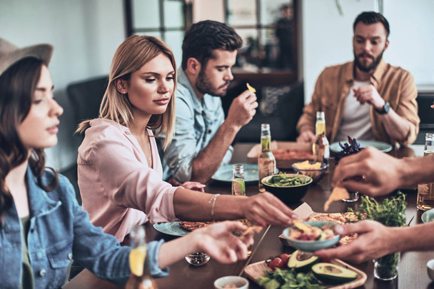 group of young people in casual clothing eating at table with beer bottles  - Foto, Imagen