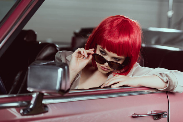güneş gözlüğü ayarlama ve araba aynaya bakarak kırmızı peruk şık kız güzel - Fotoğraf, Görsel