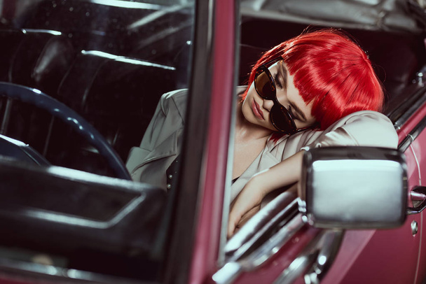 güzel genç kadın kırmızı peruk ve eski model araba uyku güneş gözlüğü - Fotoğraf, Görsel