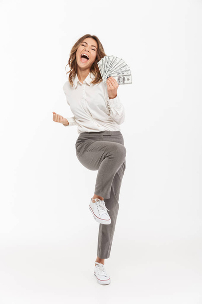 Full length portrait of an excited young business woman holding money banknotes and celebrating isolated over white background - Foto, immagini