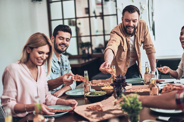 friends smiling while taking pizza slices at dinner party table with beer  - Fotoğraf, Görsel