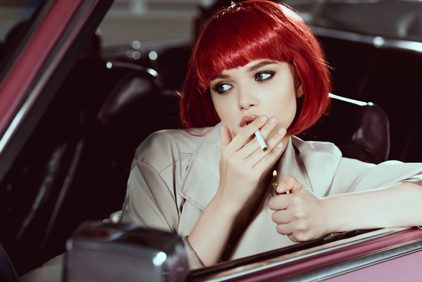 Atrakcyjna dziewczyna w czerwoną perukę papierosa i odwracając się siedząc w samochodzie  - Zdjęcie, obraz