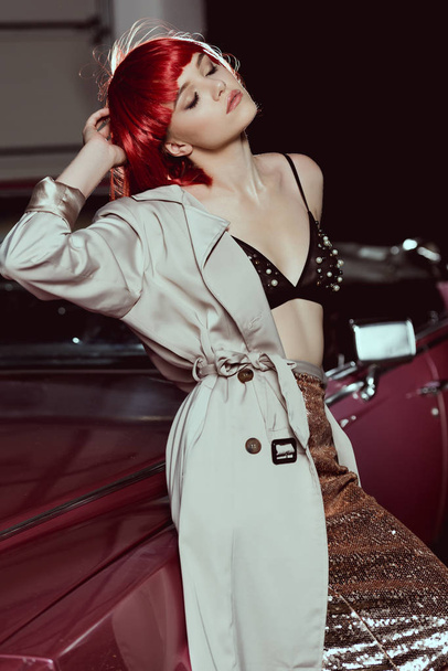 sensual girl with closed eyes wearing trench coat and leaning at classic car - Photo, Image