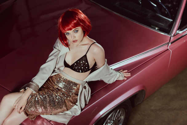 high angle view of beautiful stylish girl sitting on vintage car and looking at camera  - Fotó, kép