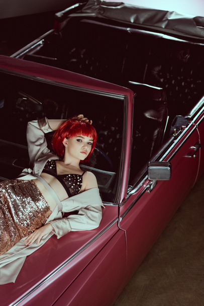 high angle view of beautiful stylish girl lying on vintage car and looking at camera  - Foto, Bild