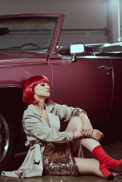 beautiful young woman in fashionable trench coat sitting near retro car  - Photo, Image