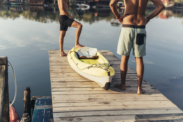 Two unrecognisable men standing by the canoe on wooden deck. - Foto, imagen