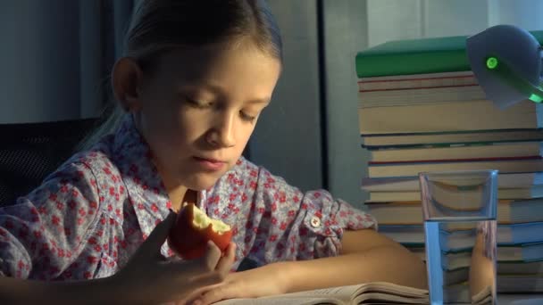Child Reading at Desk Lamp in Evening, Learning, Girl Eating Apple Studying Book - Filmagem, Vídeo