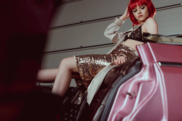 selective focus of young woman in trench coat, glittering skirt and bra sitting in retro car - Foto, Bild