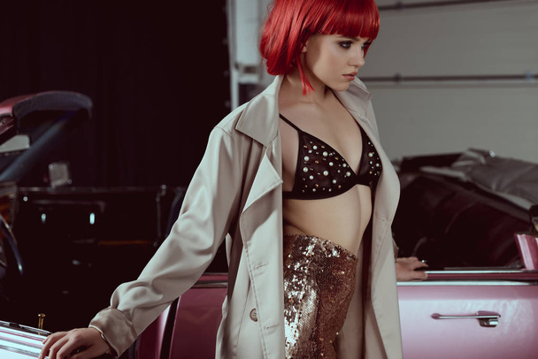 流行のトレンチ コートは、レトロな車の近くに立っている間よそ見で美しい若い女性  - 写真・画像