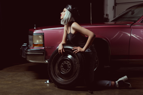 side view of sensual young woman repairing car wheel - Photo, Image