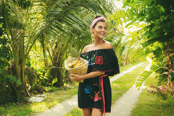 Happy young woman with basket full of exotic fruits in tropical garden - Photo, Image
