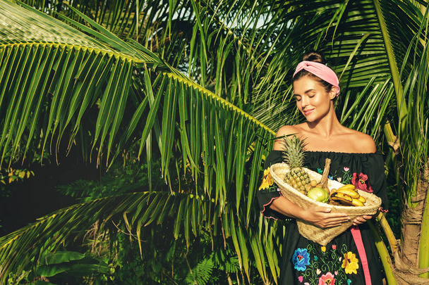 Happy young woman with basket full of exotic fruits in tropical garden - Fotografie, Obrázek