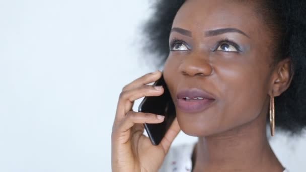Portrait of the young charming african woman with pretty smile talking on the mobile phone over white background. - Video, Çekim
