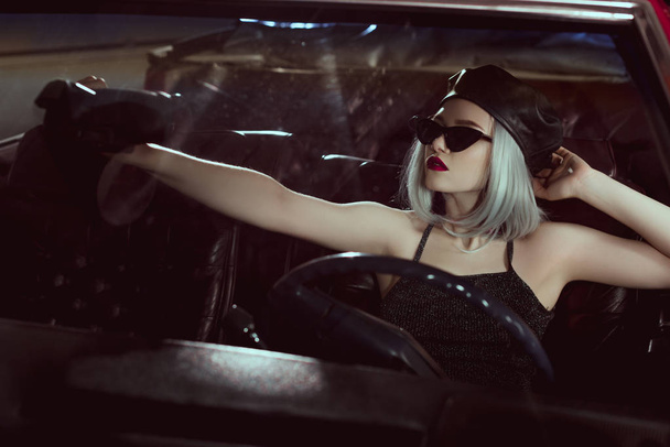 menina loira na moda em boina preta e óculos de sol sentado no carro retro
 - Foto, Imagem