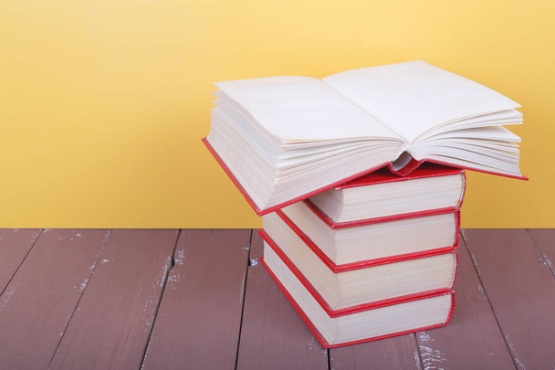Wissenschaft und Bildung - Stapel roter Bücher eine leere offene Frontansicht auf dem Holztisch und gelbem Hintergrund. - Foto, Bild