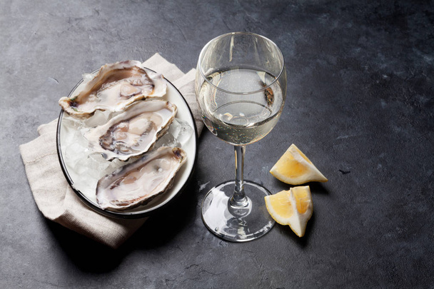 Opened oysters, ice and lemon and white wine on stone table. Selective focus on wine - Fotó, kép