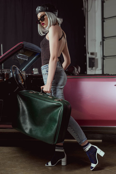 full length view of stylish blonde woman in sunglasses and beret holding old-fashioned suitcase bear retro car - Fotoğraf, Görsel