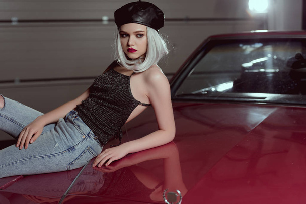 красивая стильная молодая женщина в черном берет опирается на бордовый автомобиль и смотрит в сторону
   - Фото, изображение