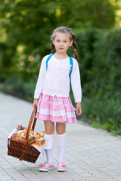 A little girl holds a lot of bread and biscuits on the street in the city. A child with a basket of bread is on the road. - Фото, изображение