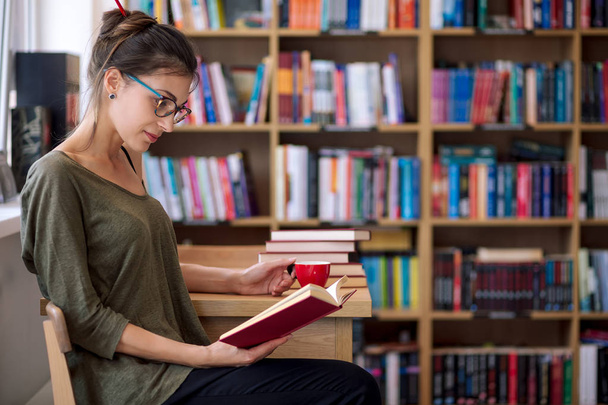 Femme avec des lunettes lisant un livre avec une tasse de café
 - Photo, image