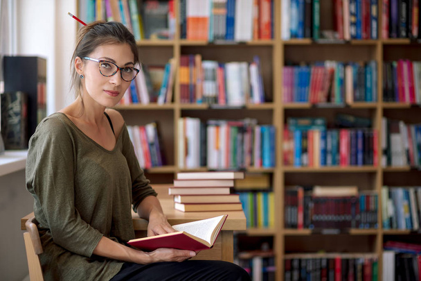 Młoda atrakcyjna kobieta trzyma książkę w bibliotece - Zdjęcie, obraz