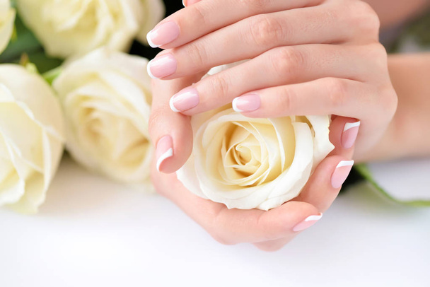 Egy gyönyörű francia manikűrös és fehér rózsás nő kezei - Fotó, kép