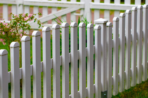 witte hek op groene gras en bloemen genomen close-up. - Foto, afbeelding