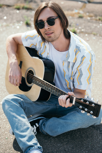 Young man playing guitar and sitting on ground in urban environment - Foto, Imagen