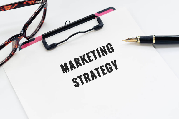 Επιχειρηματική ιδέα, Πρόχειρο με λέξη στρατηγική μάρκετινγκ, στυλό και τα γυαλιά σε λευκό φόντο - Φωτογραφία, εικόνα