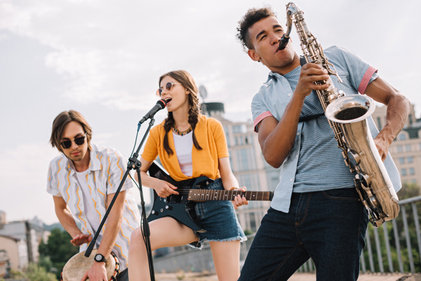 Multiracial young people with guitar, djembe and saxophone performing on street - Photo, Image