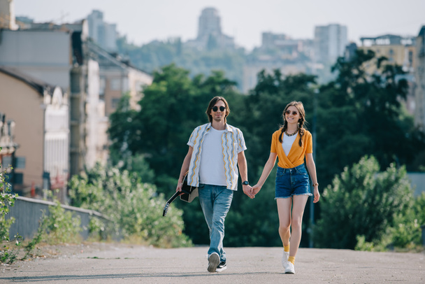 Szczęśliwa para hipster buskers spaceru i trzymając się za ręce na ulicy - Zdjęcie, obraz