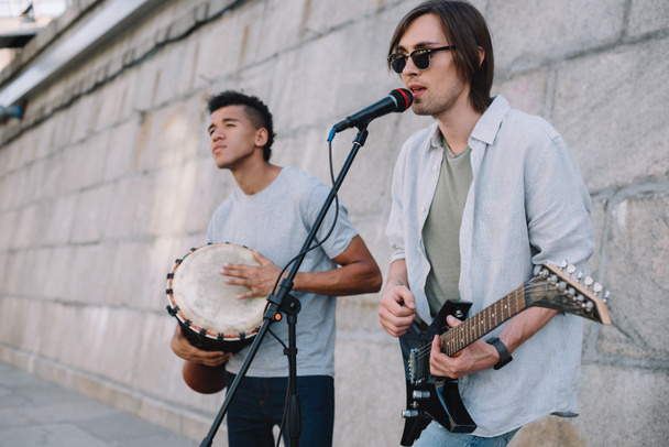 Equipe de jovens amigos multirraciais do sexo masculino tocando música e cantando em ambiente urbano
 - Foto, Imagem