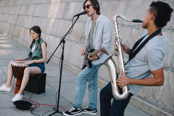 Team junger befreundeter Musiker, die im städtischen Umfeld spielen und singen - Foto, Bild