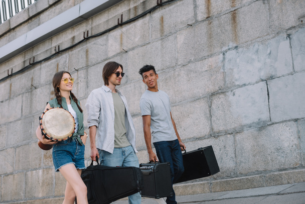 Çok ırklı müzikal grup yürüyüş ve güneşli şehir sokak üzerinde müzik aletleri taşıyan - Fotoğraf, Görsel