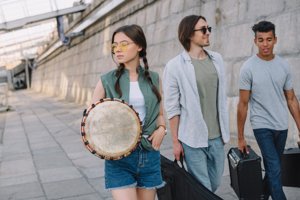 ウォーキングや都市環境で楽器を運ぶ若い男性と女性の友人のチーム - 写真・画像