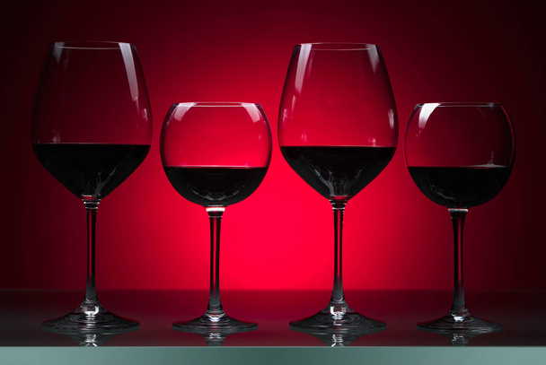 Glasses of red wine on a red background. - Φωτογραφία, εικόνα