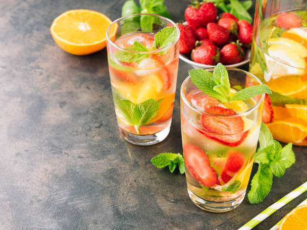 The glasses of lemon water. Lemonade with strawberry, mint and ice on a table. Sunny summer day - Foto, afbeelding