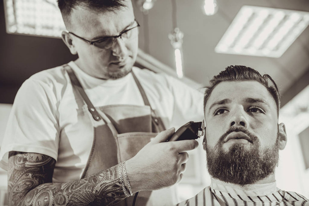 Man during trimming a beard in a barbershop in black & white stylization  - 写真・画像