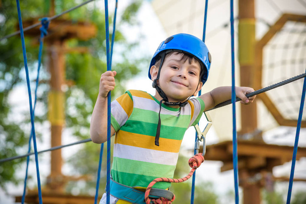 boy having fun at adventure park. toddler climbing in a rope playground structure. toddler climbing in a rope playground structure. Safe Climbing extreme sport with helmet and Carabiner - Фото, зображення