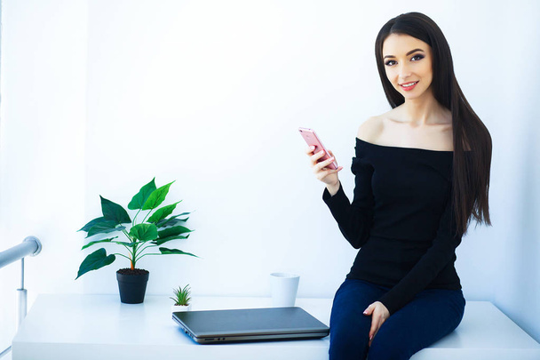 Office Business Woman Smiling and Sitting on the Table. Woman Dressed in Black Blouse and Blue Jeans. Work at Home. High Resolution - Valokuva, kuva