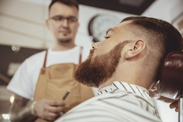 Man with beard waits for a shave with a razor in a barbershop. Photo in vintage style - Foto, Bild