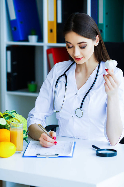 Health. Diet and Healthy. Nutrition. Portrait of a Dietitian's Doctor with Fresh Fruits and Vegetables. Beautiful and Young Doctor in the Light Room Holding in Garlic Hands. High Resolution - Zdjęcie, obraz