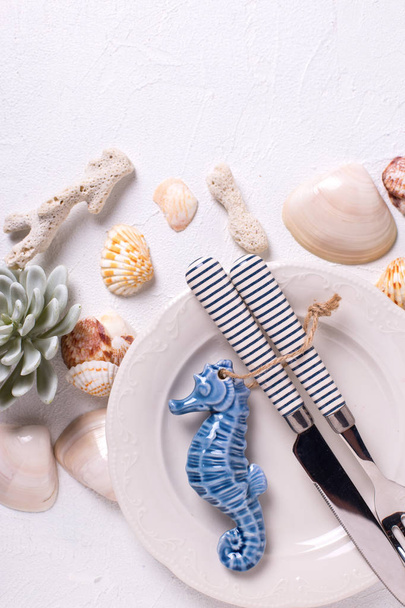 Nautical  elements and white plate on white textured  background. Shells, cutlery, sea star, coral, sea horse, succulent echeverial. View from above. - Photo, Image