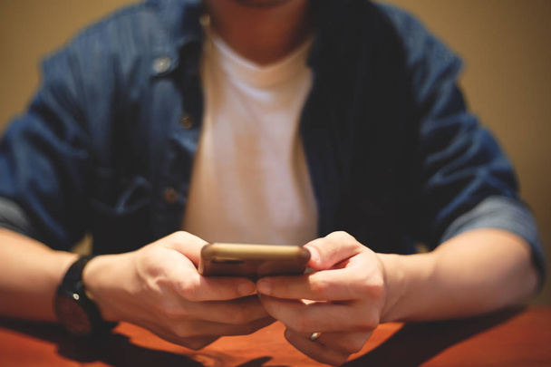 Hipster młody człowiek za pomocą smartphone siedząc w kawiarnia vintage tonem. Zamknij się człowiek ręka trzymać i dotykając ekranu telefonu komórkowego dla bankowości online, przeczytać wiadomość, Wyślij sms. - Zdjęcie, obraz