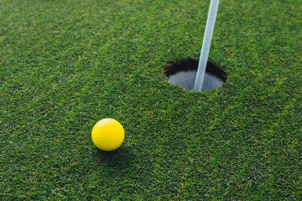 keltainen golf pallo lähellä reikä pin lippu, vihreä ruoho tausta, lähikuva
 - Valokuva, kuva