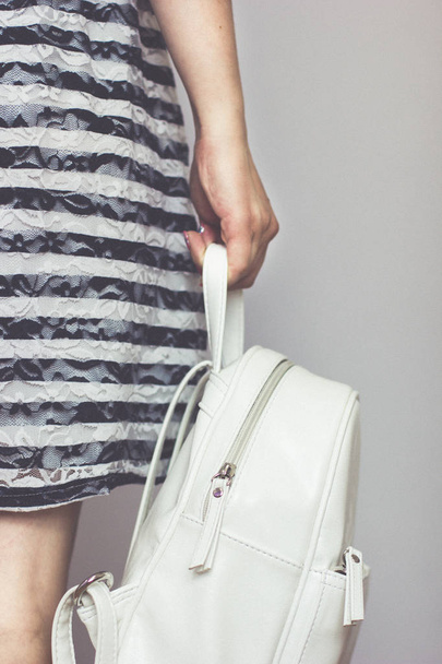 young girl in a striped dress is holding a white backpack. - 写真・画像