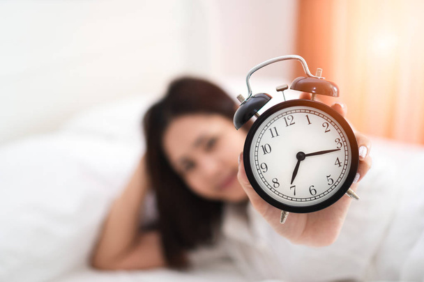 Close up alarm clock having a good day with young happy asian woman hand raising black alarm clock enjoying waking up in early morning on bed after fully sleeping. Rest, relax, lifestyle and weekend. - Foto, Imagem